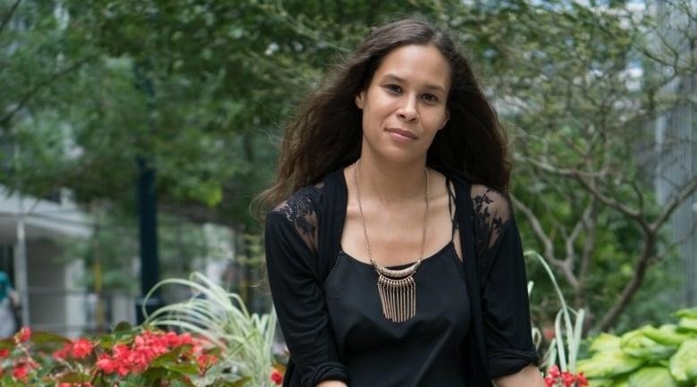 A Black woman with long hair sits on a bench amid flowers.