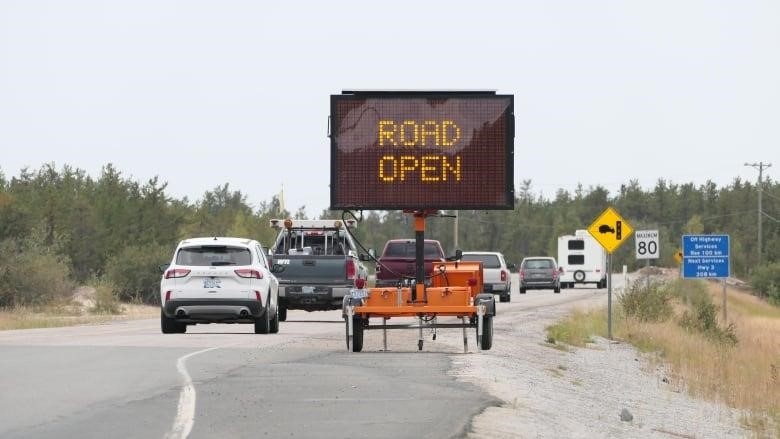 Vehicles on a highway behind a sign saying "Road Open".