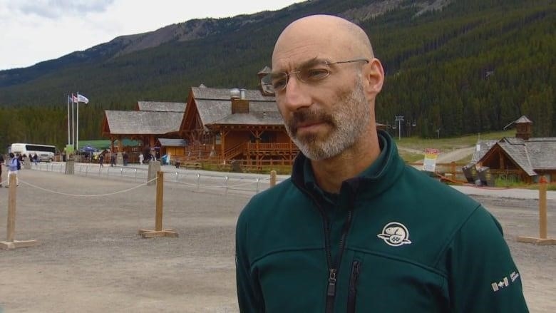 A man wearing a green Parks Canada jacket looks off screen. 