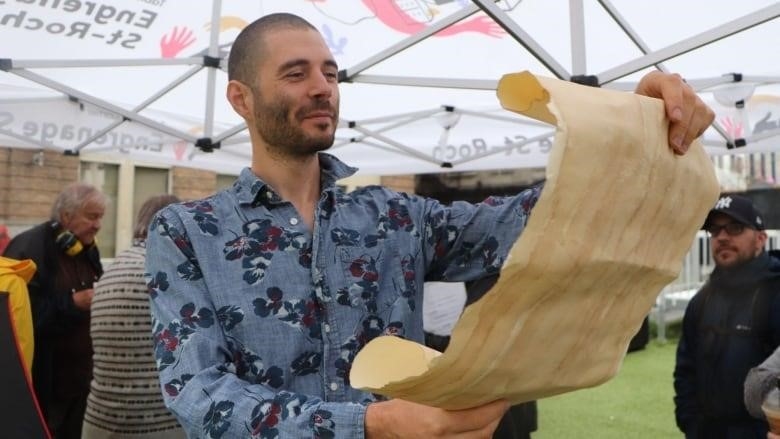 A man reads from a scroll of paper 