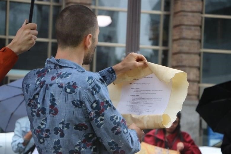 A man reads from a paper scroll.