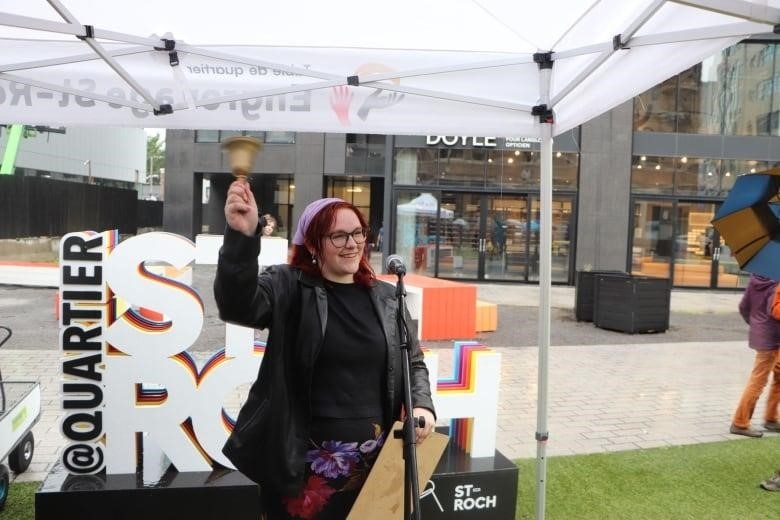 A woman rings a bell in front of a sign that says St-Roch 