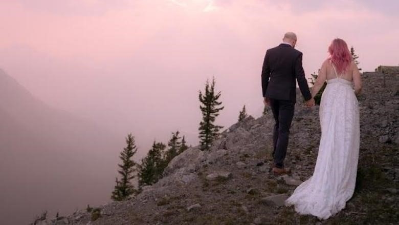 A couple holds hands. The woman is in a wedding dress. 