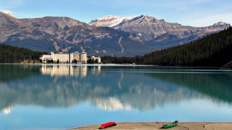 The Fairmont Hotel is reflected in clear blue water with mountains behind. 