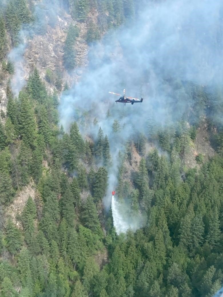 A helicopter drops a bucket of water on a smoky forest.