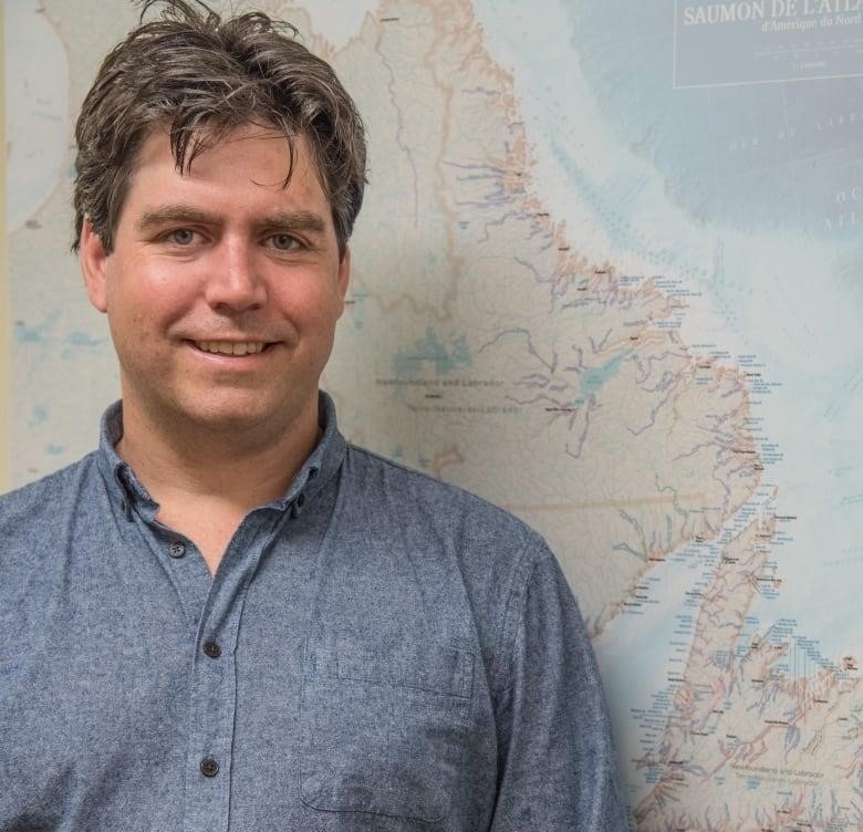 A man with brown hair stands in front of a map of Newfoundland and Labrador.
