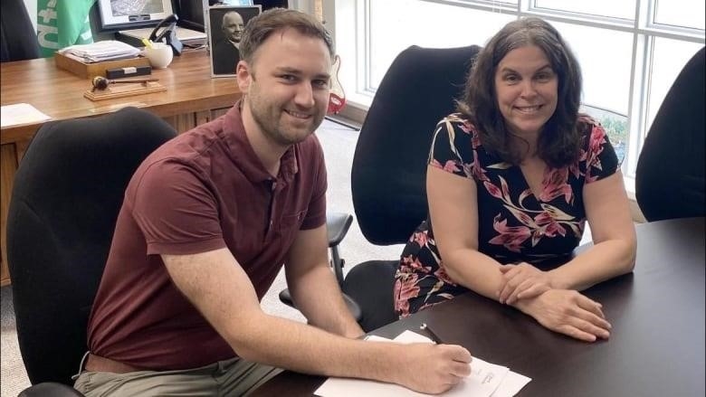 Nancy Peckford and Roderick MacPhee sign papers on a table.