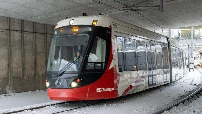 A red and white light rail train goes under a bridge in winter.