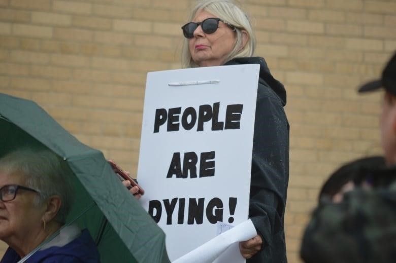 A woman holds a sign that says people are dying help