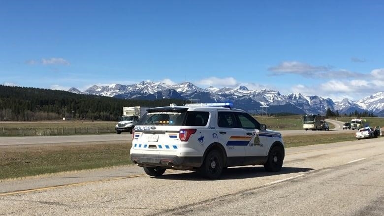 A white-and-blue police cruiser on a highway with snow-capped mountains in the distance. 