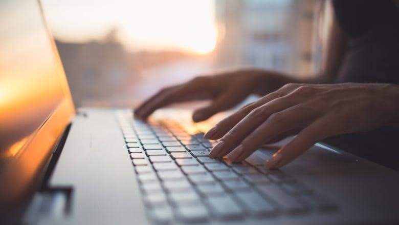 A closeup shows a woman's hands on a laptop keyboard in a sunlit room.