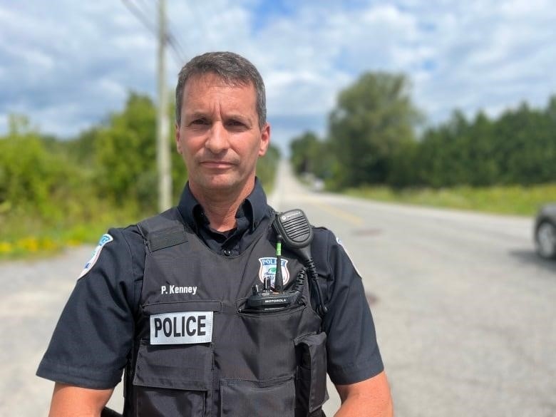 A man standing wearing a police officer uniform and vest. 