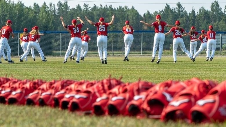 The Canadian national women's baseball team does jumping jacks on a baseball field.