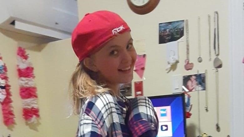 A girl in a red baseball cap smiles at the camera.