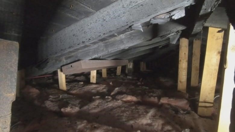 Soot lays on pink insulation in an attic that is encased in blackened wood. There is a rusty metal casing where a light once was. 