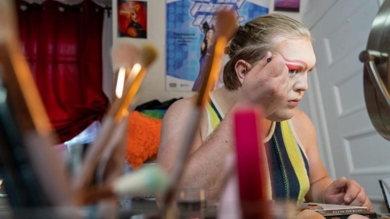 A portrait of a person applying makeup to their face in front of a mirror.