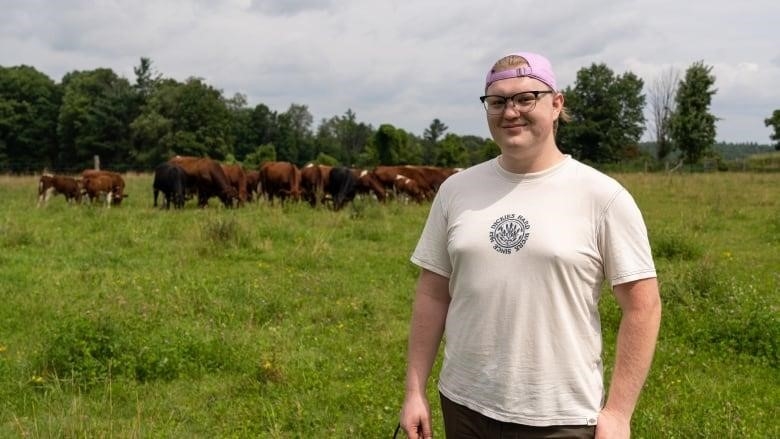 A portrait of a young person in front of a field of cows. 